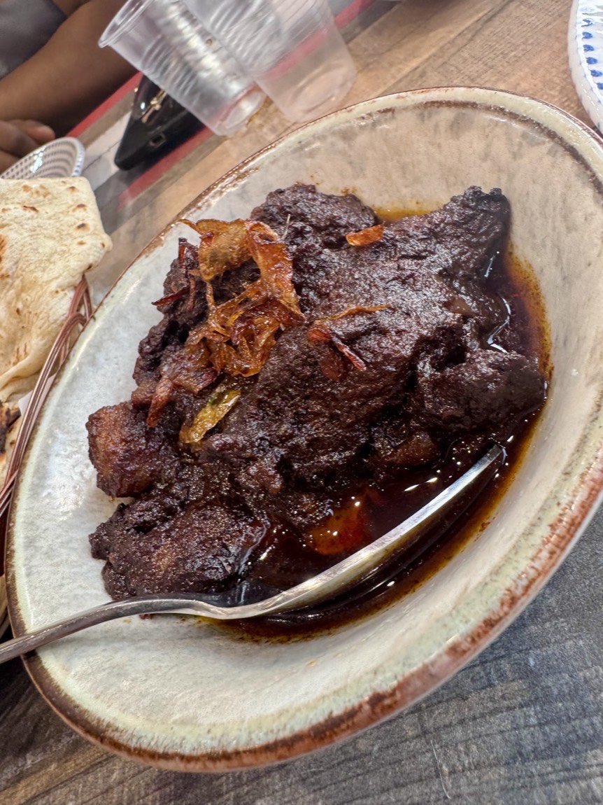 Dark, rich beef kala bhuna in a stone bowl at Lobongo, topped with crisp fried onions.