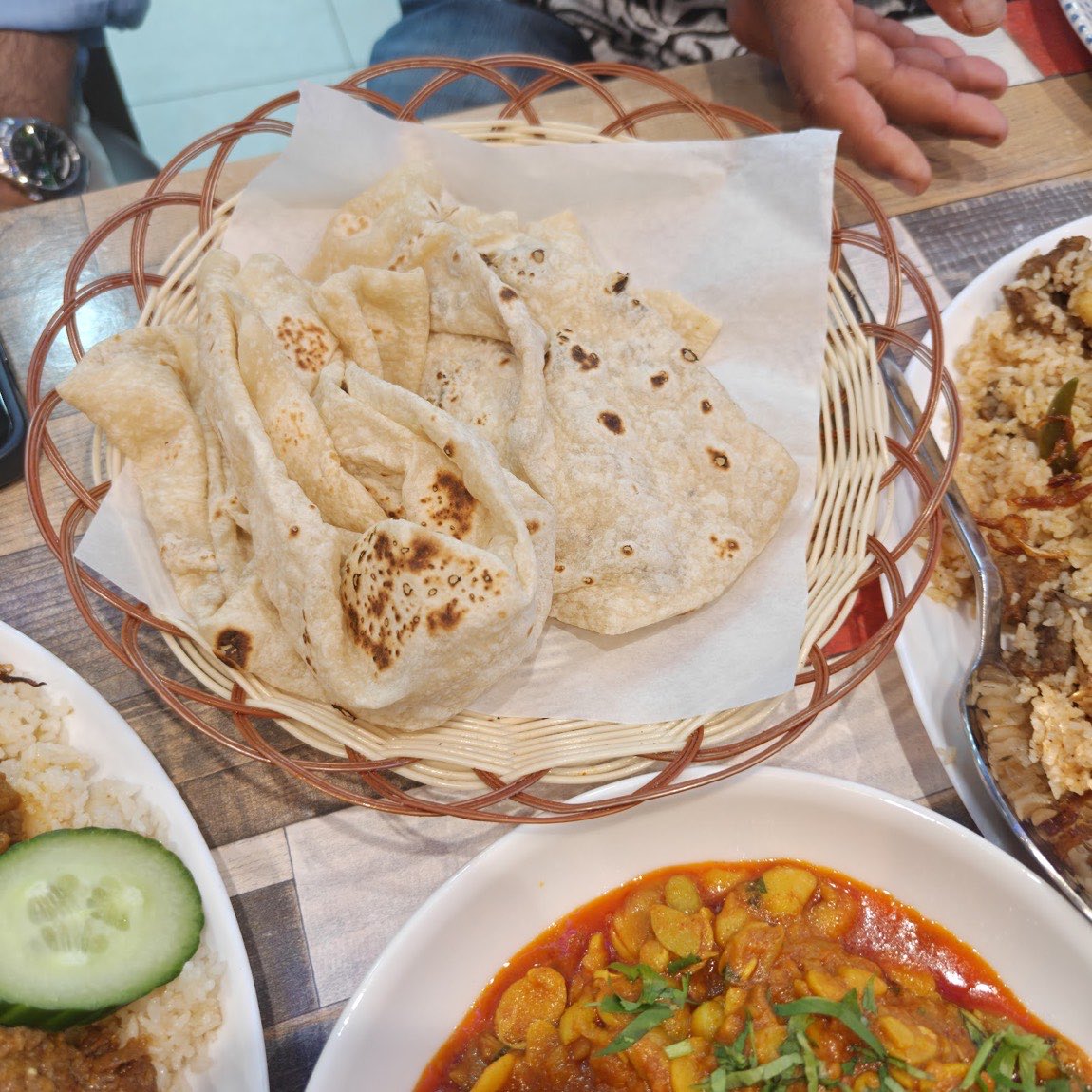 A basket of freshly made roomali roti and paratha breads on the table at Lobongo, with rice and curry alongside.